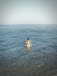 Rear view of woman wearing bikini standing in sea against clear sky