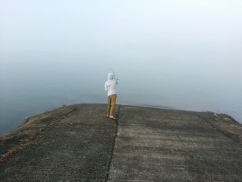 Rear view of person fishing at jetty during foggy weather