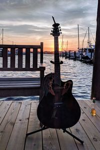 View of guitar on wooden post by pier against sky during sunset