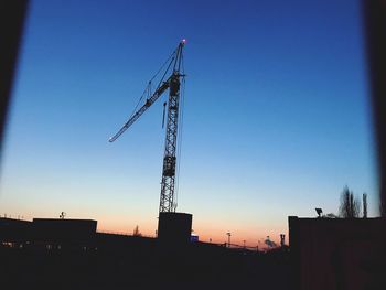 Low angle view of silhouette crane against clear blue sky