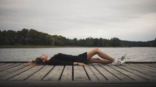 Woman lying on pier over lake against sky