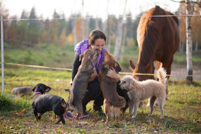 Mid adult woman playing with dogs while crouching on grassy field