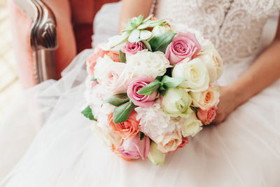 Midsection of bride wearing wedding dress while holding bouquet