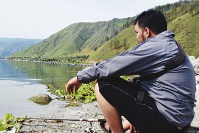 Rear view of man looking at lake against mountain