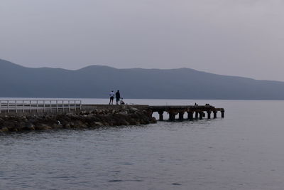 People fishing on sea by mountains against sky