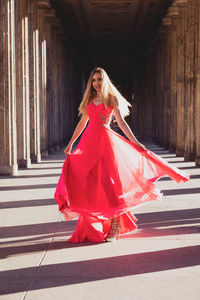 Full length portrait of young woman in pink evening gown standing at colonnade