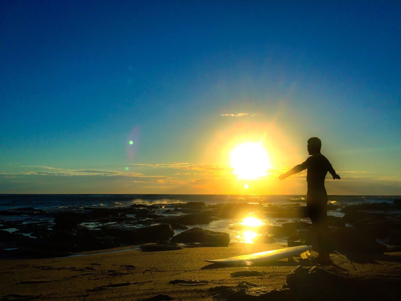 sea, water, beach, sunset, leisure activity, sun, horizon over water, lifestyles, shore, standing, silhouette, full length, beauty in nature, sky, sunlight, scenics, tranquil scene, nature