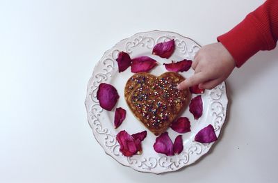 Cropped hand of child touching cake over white background