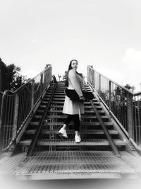 Woman standing on footbridge against sky