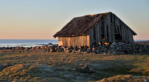 Stilt house by sea against clear sky during sunset