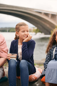 Smiling girl looking away while holding drink on lakeshore with family in park during picnic