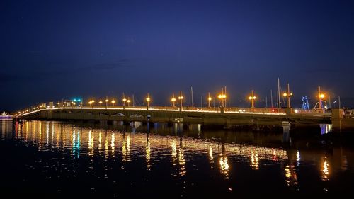 Illuminated bridge over river against sky at night