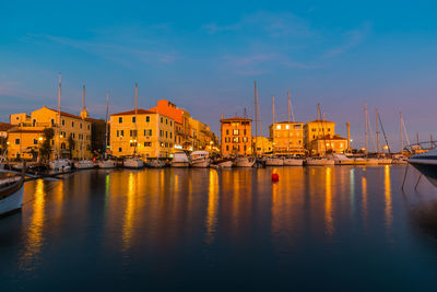 Sailboats moored in sea by buildings against sky in city