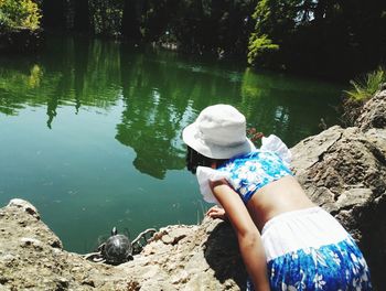 Rear view of girl looking at tortoise in lake during sunny day