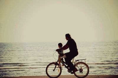 Man with bicycle on sea at sunset