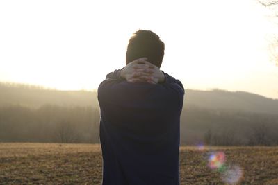 Rear view of man standing on field against sky during sunset