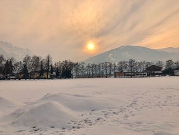 Snow covered land and mountains against sky during sunset