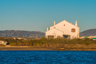 Buildings by sea against clear blue sky