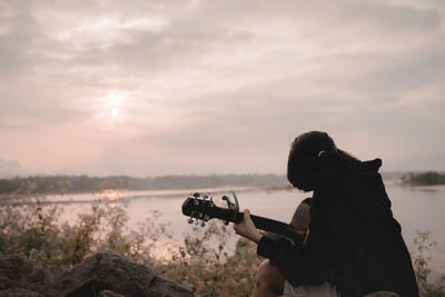 Rear view of man photographing with camera against sky during sunset