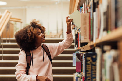 Side view of woman using mobile phone while standing in library