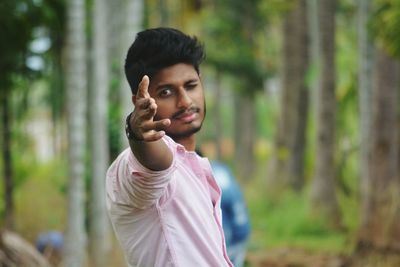 Portrait of young man gesturing while standing against trees in forest