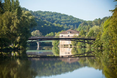 Arch bridge over lake by house and trees against sky