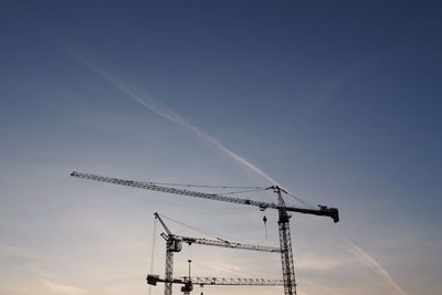 Low angle view of silhouette cranes against sky at sunset