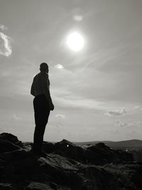 Shirtless man standing on rock against sky during sunset