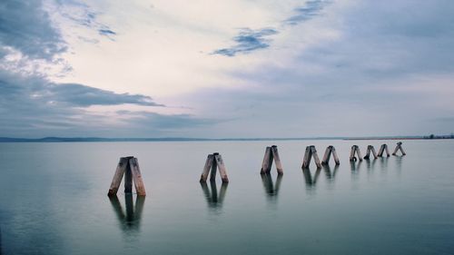 Wooden posts in sea against sky
