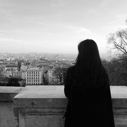 Rear view of woman looking at cityscape against sky