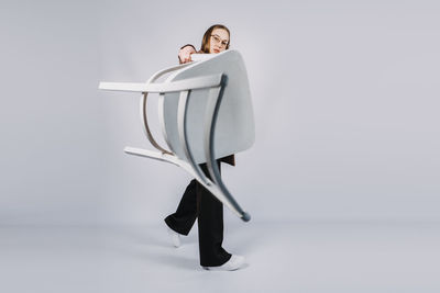 Full length studio portrait of exciting young woman fashion designer, stylist with white chair