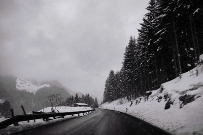 Road amidst snow covered trees against sky