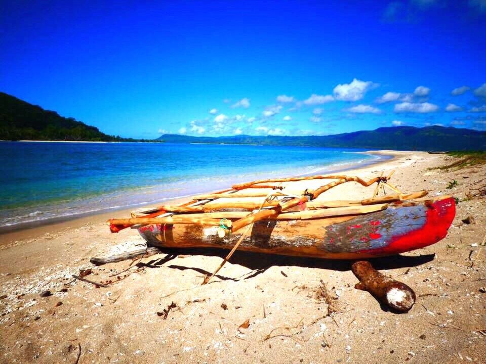 BOAT MOORED ON SHORE AT BEACH AGAINST SKY