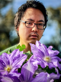 Close-up portrait of young man behind large purple clematis flowers.