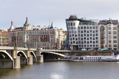 Bridge over river by buildings against sky in city