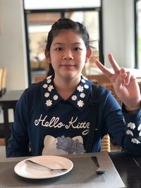 Portrait of girl showing peace sign while sitting in restaurant