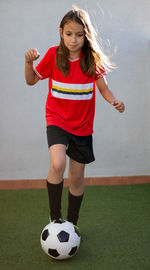 Full length of girl playing with soccer against wall