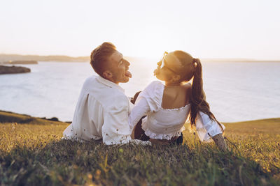 Friends sitting on shore by sea against sky