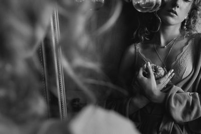 Midsection of young woman holding orange while standing by mirror at home