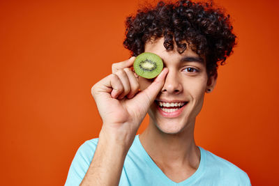 Portrait of smiling young man holding apple against orange background