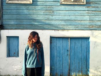 Portrait of young woman standing against house