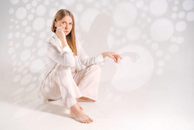 Thoughtful woman sitting her head light clothes white background with light