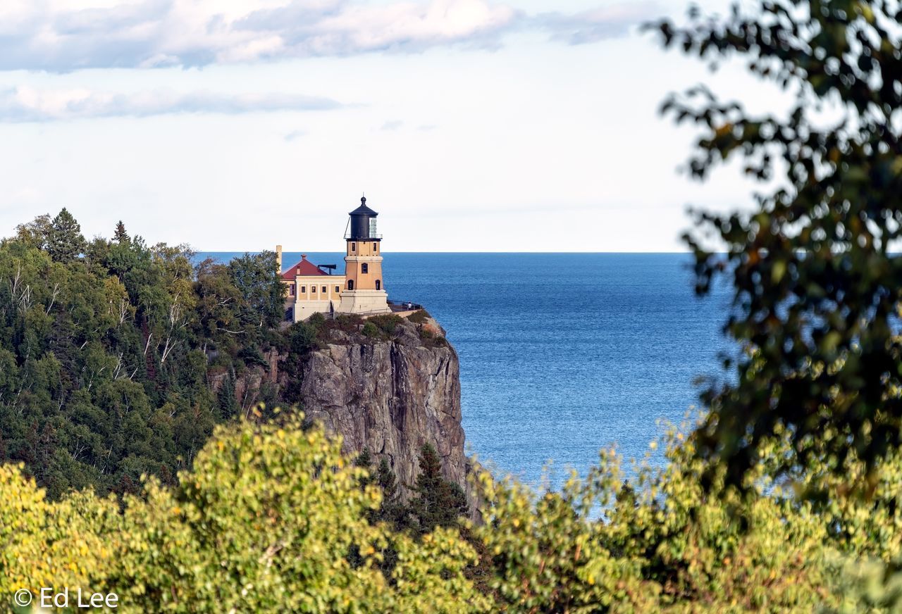 LIGHTHOUSE BY SEA AGAINST BUILDINGS