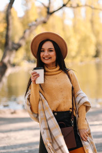 Beautiful smiling girl in casual clothes drinking coffee walking in nature in autumn outdoor