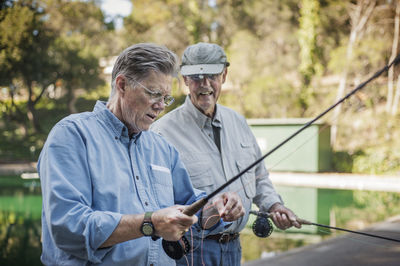 Happy senior male friends holding fishing rods in forest