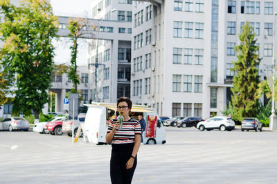 Side view of woman using mobile phone with smoothie in her hands in city against clear sky