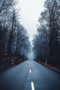 Road amidst bare trees against clear sky