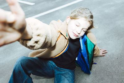 Girl in warm clothing with eyes closed sitting on street