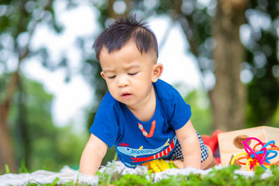 Cute boy crawling by toys on grass