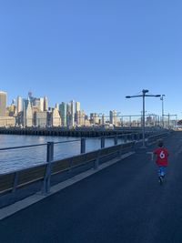 Rear view of boy walking by river on road in city